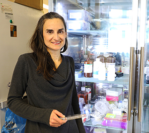 Laura Heiser, Ph.D. stands near a clear glass refrigerator in her lab