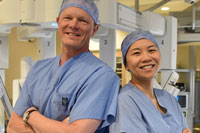 A man and a woman, both in hospital scrubs, smiling while standing back-to-back with their arms crossed.