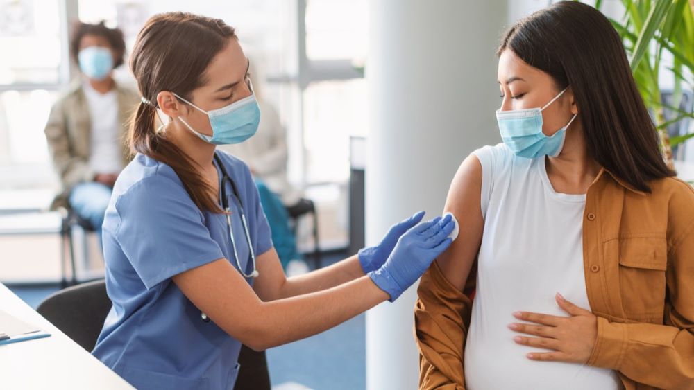 A pregnant person receives an RSV shot from a nurse in blue scrubs.