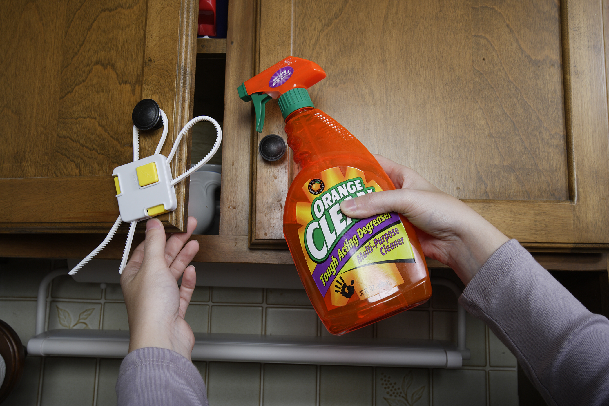 Safe storage of a household cleaning product is demonstrated as an orange spray bottle is placed in an upper cabinet with a cabinet lock to prevent poisonings