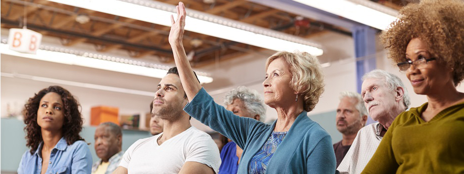 A group of people sitting in rows, with one woman raising her hand.