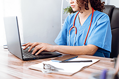 Woman nurse sitting at a desk and typing on a laptop.