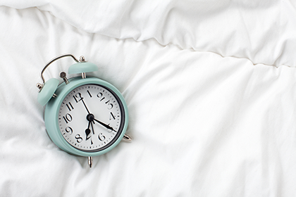 Picture of an analog alarm clock on a bed.