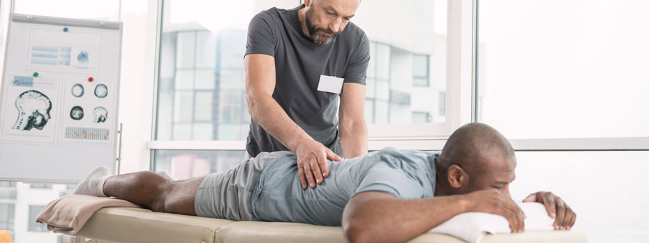 A person with cancer is lying down and getting a back massage from a therapist in a clinic.