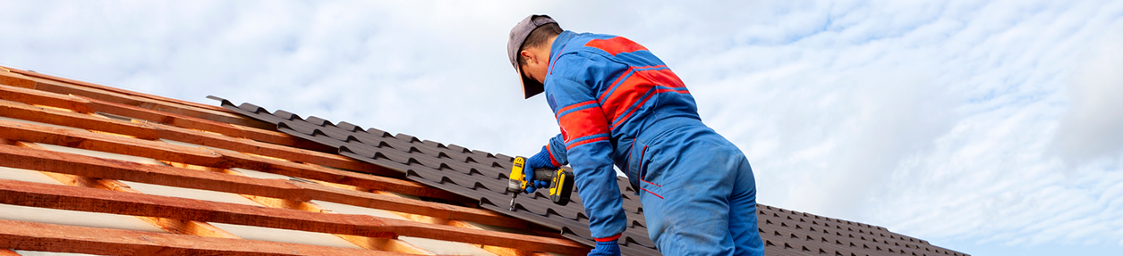 Man worker uses a power drill to attach a cap metal roofing job with screws.