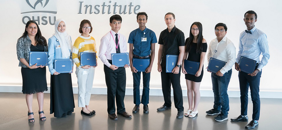 Nine people standing in a row, each holding a certificate in front of a wall with the OHSU logo on it.