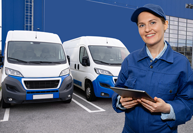 Woman worker wearing blue uniform is holding digital tablet and looking at the camera. Vans are parked in row. Vans are parked in row. Commercial fleet
