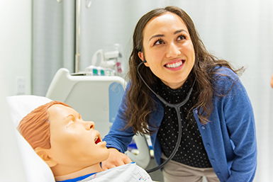A nursing student smiles off camera while working with a manikin in the simulation lab