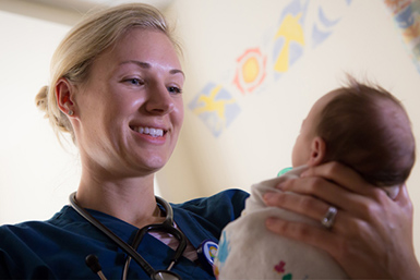 A nursing student holds a newborn baby and smiles