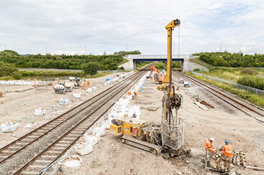 Construction workers, and pile drilling machine, on site next to a section of railway track