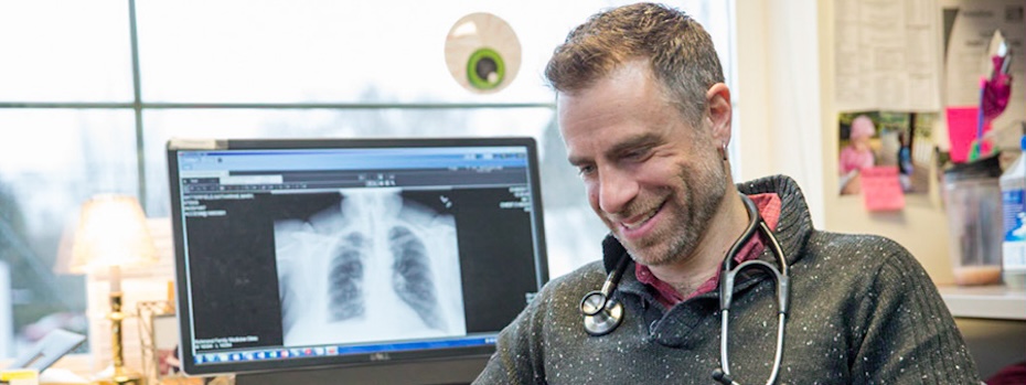 Dr. Brian Frank smiles while sitting in his office by a computer showing a chest X-ray at OHSU Primary Care Clinic, Richmond.