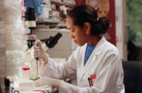 Black woman in a lab coat pipetting near a microscope in a laboratory.