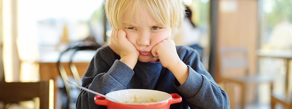 A young boy looking upset in a kitchen with food in front of him