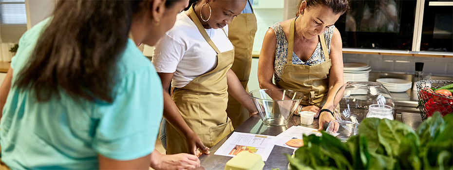 Students in a kitchen classroom work together on a hands-on nutrition lesson, preparing ingredients and following a recipe.