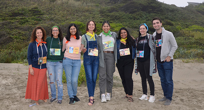 A group of doctors in casual attire standing next to each other smiling at the beach.
