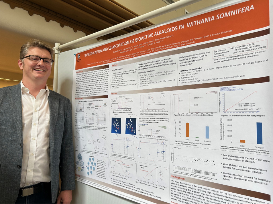 A man in a gray tweed blazer stands smiling in front of his scientific poster.