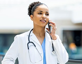 A female doctor holds a cellphone to her ear and listens.