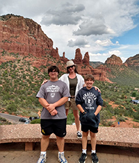 A woman standing behind her two teenage sons with large red rock formations behind them.