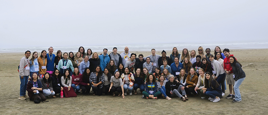 A group of approximately 50 people standing and crouching together on the beach on a cloudy day.