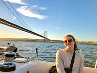 A woman smiling on a boat with a bridge visible behind her on a sunny day.