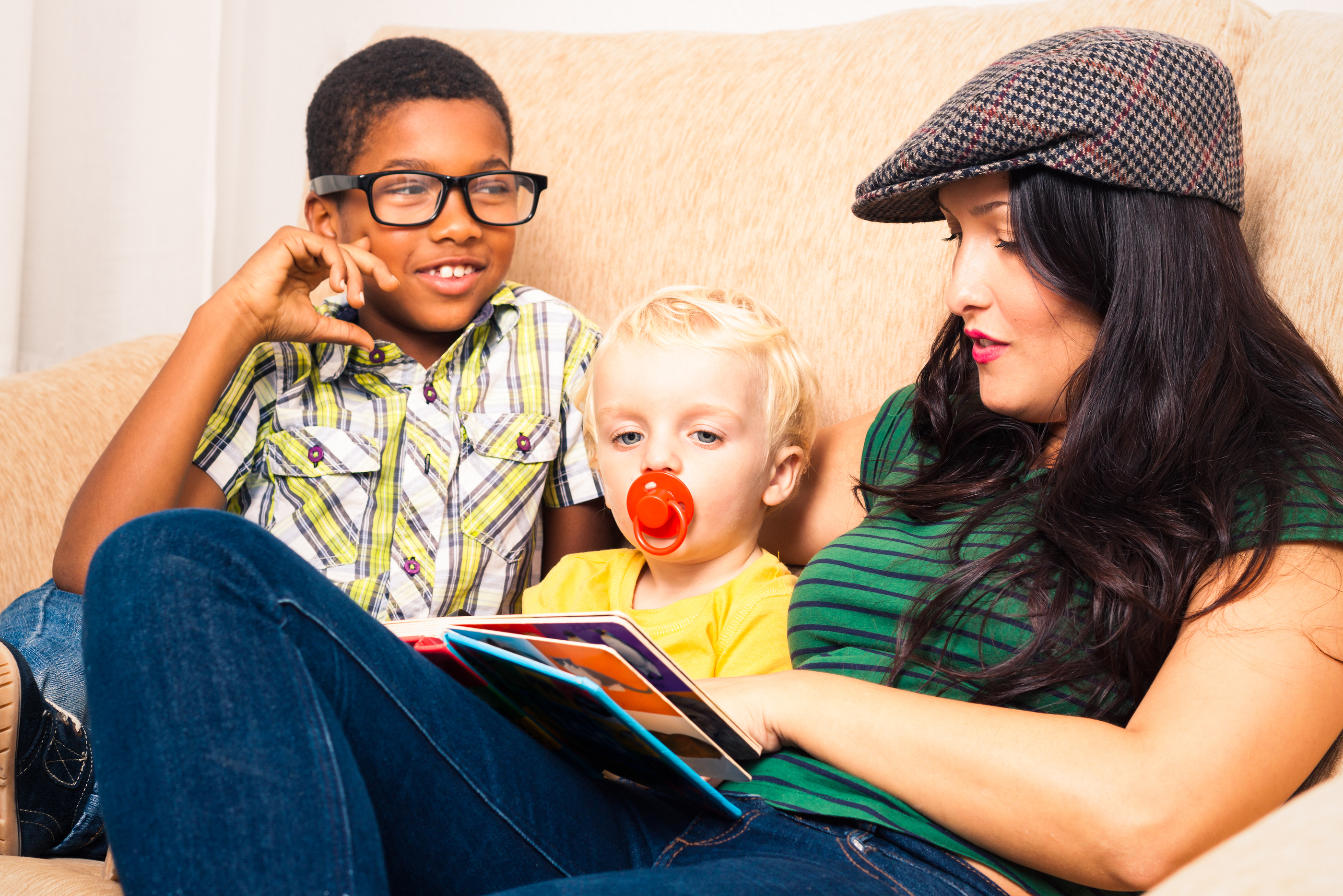 Young child and toddler sitting on a coach being read to by a young woman, different races.