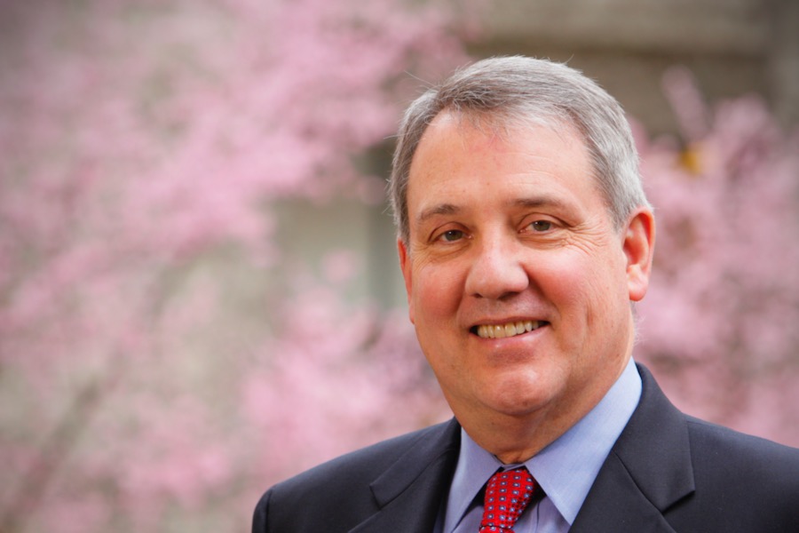 Former OHSU President Joe Robertson smiles at the camera in a portrait from the shoulders up. A tree filled with pink blossoms is the backdrop.