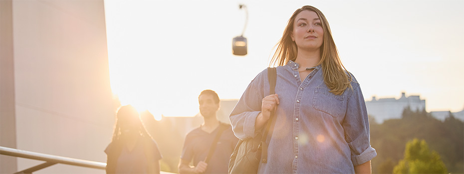 Student walking across OHSU campus bridge at sunset with fellow students and the OHSU tram in the background.