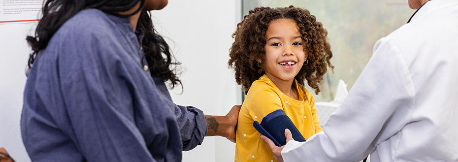 A child gets her blood pressure measured at the doctor’s office while her mom watches.