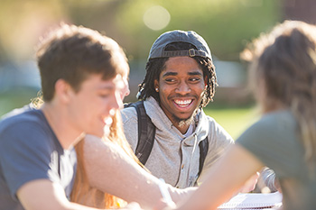 A student smiles while sitting outside in a group.