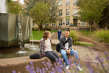 Two students sitting along the fountain in front of Mac Hall.