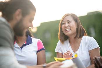 A student takes notes as she talks with others.