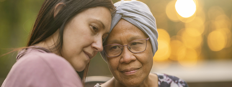 A young woman and an older woman wearing a turban stand side by side with their foreheads touching.