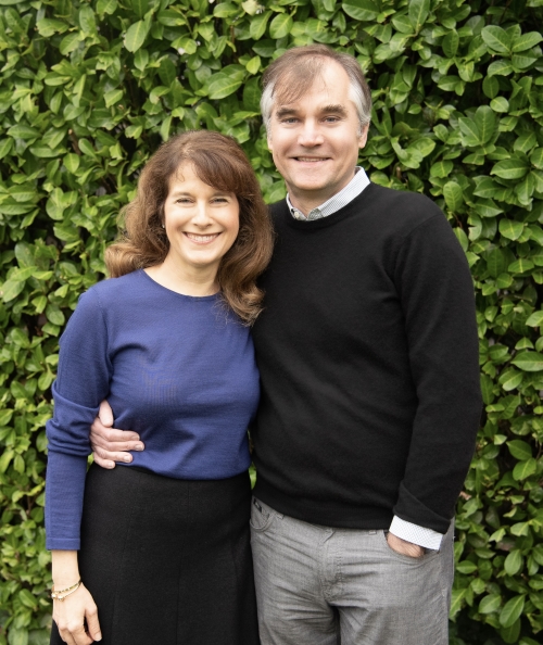 A husband and wife couple stand together smiling at the camera.