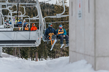 Skiers and snowboarders ride the lift above a snowy mountain landscape.