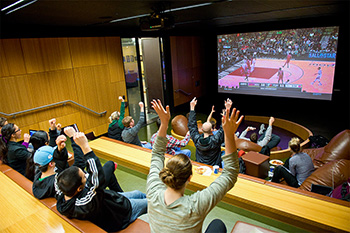 Students cheer as they watch a basketball game in the Student Center's media room.