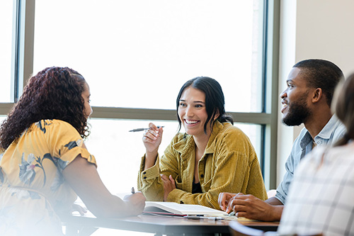 Three students smile while chatting around a table.
