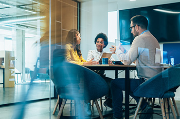 Three faculty members having a discussion at a conference table in an office.