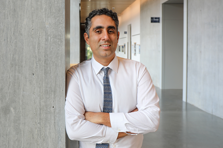 A man smiles standing with his arms crossed leaning against a wall in a hallway.