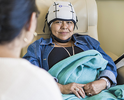A patient wears a helmet-like cap while sitting with another person.