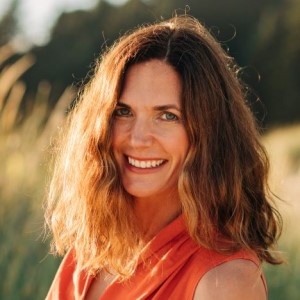 Jana Peterson-Besse, a woman in her 40s with shoulder-length brown hair wearing an orange top, pictured outside in warm sunlight
