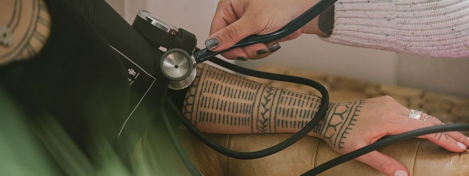 An OHSU nursing student performs a blood pressure check on a patient’s arm with traditional Indigenous tattoos.