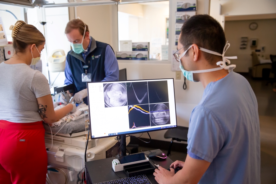 Three people surround a baby's bedside to take a non-invasive image of the retina.