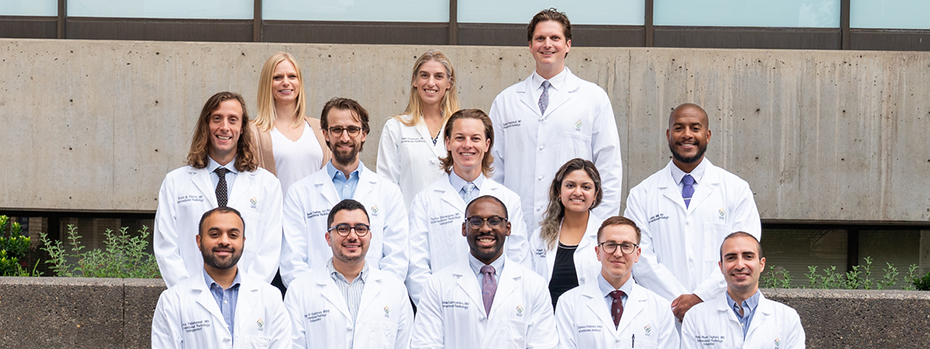 Group of medical residents in white lab coats posing together outdoors in front of a concrete building
