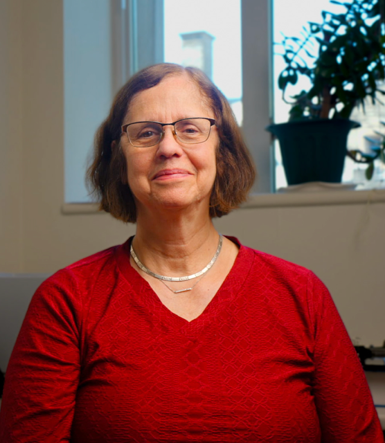 A portrait photo of Victoria P. Werth, M.D.: A woman smiles for a photo indoors in front of a window and plants