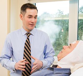 Dr. Paul Motika, neurologist at OHSU, talks to a patient in a bed at OHSU’s epilepsy monitoring unit.
