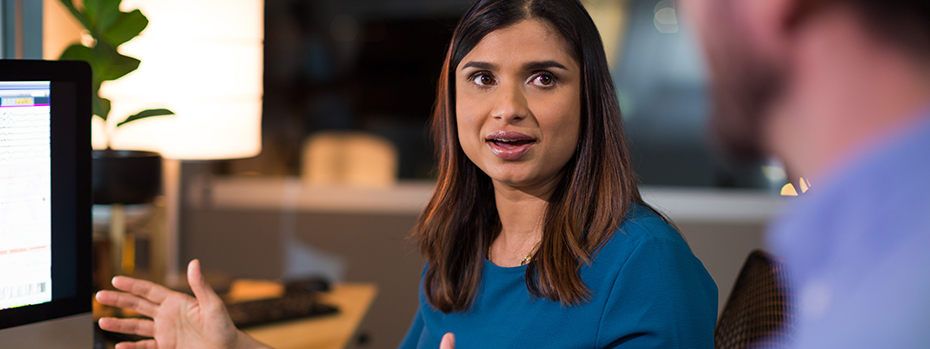 Dr. Asha Singh sits at her desk talking to a colleague