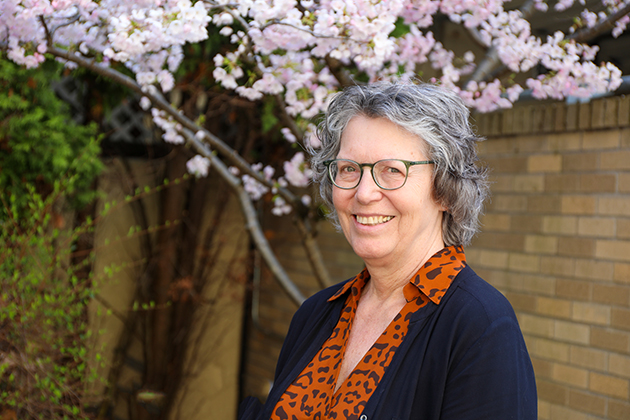 A portrait of a smiling Fay Horak in front of a blooming cherry tree and brick building on OHSU’s campus.