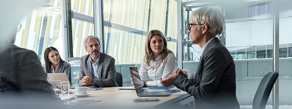 A group of health care and business professionals engaged in a leadership discussion around a conference table in a meeting room.