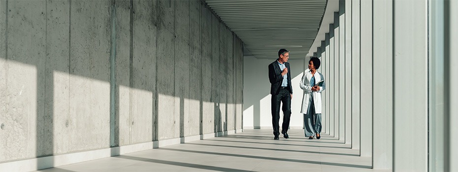 Two health care professionals engaged in conversation walk together through a corridor.