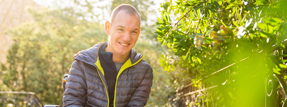 Young man outside in a wheelchair smiling on a sunny day.]